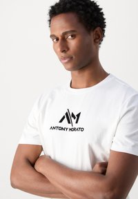 T-shirt en coton blanc avec un logo imprimé noir "ANTONY MORATO" sur la poitrine. Manches courtes et col rond. Texture lisse.