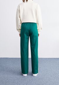 Gröna träningsbyxor med vita ränder och lös passform, tillverkade av mjukt tyg. Har en elastisk midja och ribbade mudd.