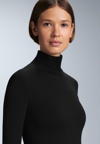 Čierny rolák vyrobený z hladkej pleteniny, s priliehavým strihom a rebrovanou textúrou na golieri, predvádza elegantný siluetu.