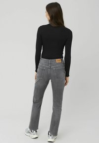 Jean en denim gris avec une coupe droite, comportant deux poches arrière et une étiquette en cuir marron. Associé à un haut noir ajusté à manches longues et des baskets.