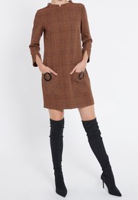 Brun rutig mini-klänning med trekvartsärmar, två runda fickdetaljer, och i kombination med svarta höga stövlar.