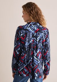 Camicia button-up nera, con un motivo geometrico rosso, blu e bianco. Maniche lunghe, vestibilità comoda e tessuto morbido.