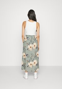 Falda maxi floral en verde con peonías crema y acentos azules, combinada con una camiseta sin mangas blanca y zapatillas blancas. Tejido de mezcla de algodón.