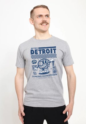 Šedé bavlněné tričko s modrou grafikou, která zobrazuje text "RETRO DETROIT" spolu s karikaturní postavou basketbalisty a ilustracemi spojenými se sportem.