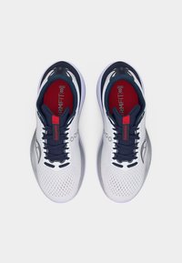 Ζευγάρι λευκά και ναυτικά αθλητικά παπούτσια με κόκκινες εσωτερικές σόλες με την ετικέτα "FORMFIT" και μαύρα κορδόνια, σε θέα από ψηλά σε απλό φόντο.