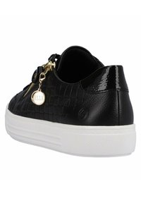 Baskets noires avec une texture tissée, des accents brillants et une semelle en caoutchouc blanche. Présente un charme doré et un détail de fermeture éclair sur le côté.