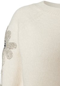 Weißer Strickpullover mit strukturierter Oberfläche und floralem Design mit silbernen Verzierungen am linken Ärmel.