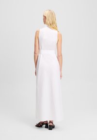 Robe blanche sans manches avec un corsage ajusté, une taille ceinturée et une silhouette A-line longueur sol. Tissu lisse avec un minimum de détails.
