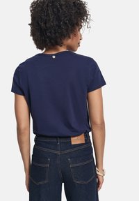 Camiseta de color azul marino con mangas cortas, con un escote redondo y un pequeño detalle de botón en la parte posterior. Combinada con jeans de mezclilla oscura.
