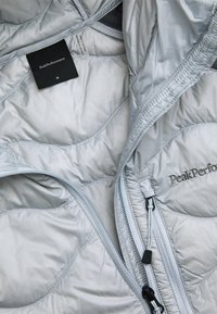 Light grey quilted jacket with zipper and chest pocket, showing Peak Performance logo and size M label inside collar.