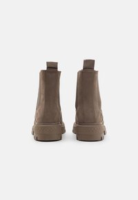 Bottes brunes à la cheville en daim, avec des panneaux latéraux en élastique, des languettes de tirage et des semelles en caoutchouc texturé. Vue arrière montrant les détails de couture.