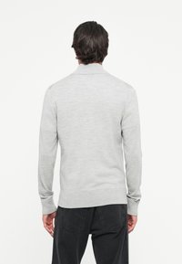 Lichtgrijze gebreide trui met een hoge kraag, lange mouwen en een geribde onderrand en manchetten. Heeft een gladde textuur en een minimalistisch ontwerp.