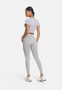 Szara krótka koszulka i dopasowane legginsy, w dopasowanym fasonie, o miękkiej fakturze, bezszwowe wykończenie, noszone z białymi sportowymi butami.