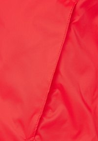 Tejido sintético rojo con una textura suave, que presenta una costura diagonal. La superficie parece ligeramente brillante con un patrón consistente.