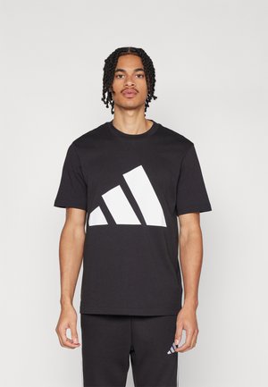 Černé bavlněné tričko s velkým bílým diagonálním logem se třemi proužky na přední části, kulatým výstřihem a krátkými rukávy.