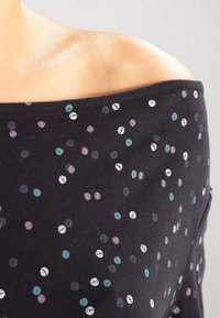 Svart off-shoulder topp med prickigt mönster i vitt, teal och lila; gjord av mjukt tyg med en avslappnad passform.