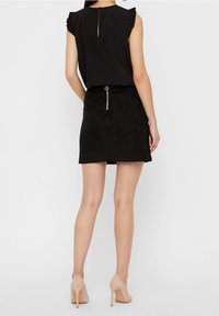 Svart ärmlös topp med volangärmar och nyckelhål i ryggen. Svart mocka minikjol med dragkedja i ryggen och cirkulärt spänne. Beiga högklackade skor.