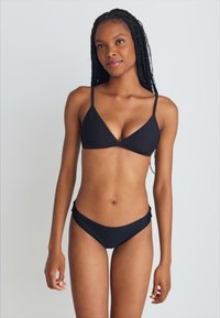 Melna bikini komplekts, kas sastāv no trīsstūra krūštura un zema jostas apakšdaļas, izgatavots no gludas tekstila ar plānām regulējamām siksnām.