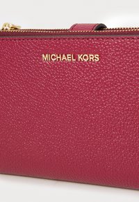 Fuchsia leather wallet with a textured finish, featuring a gold "MICHAEL KORS" logo and a gold zipper closure along the top.