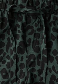 Zelená tkanina s černým leopardím vzorem, s vázacím páskem a měkkou texturou. Detaily zahrnují sklady a akcenty šití.