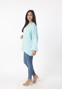 Helles blaues, übergroßes Sweatshirt aus weichem Strickstoff, kombiniert mit dunklen Skinny-Jeans und klaren Blockabsatzsandalen.