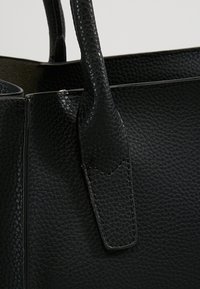 Gros plan sur une poignée de sac à main en cuir noir texturé attachée au corps du sac avec des détails de couture visibles.