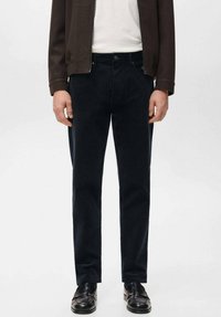 Vaqueros de mezclilla azul oscuro con un corte recto clásico, con cierre de botones y diseño de cinco bolsillos, combinados con zapatos de cuero negro.