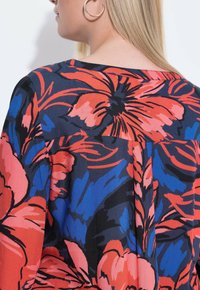 Blusa floreale con sfondo nero, caratterizzata da grandi fiori rossi e blu, maniche corte e scollo a barchetta. Tessuto morbido e leggero.