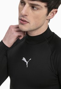 Fekete, hosszú ujjú sportpóló magas gallérral, fehér Puma logóval a mellkason. Simaság és rugalmasság jellemzi, lapos varrásokkal.