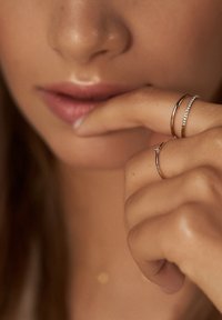 Drei Ringe an einer Hand: ein dünner Goldring, ein Goldring mit einem kleinen Diamanten und ein Goldring mit einer Reihe kleiner Steine, alle glänzend.