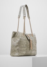 Grå handväska med krokodilsmönster och kedja, har en dekorativ lås av guld och en texturerad yta.