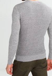 Maglione grigio lavorato a maglia con una finitura testurizzata, scollatura rotonda e maniche lunghe aderenti, abbinato a pantaloni verde oliva.