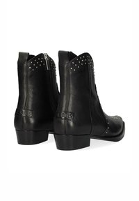 Botas de cuero negras hasta el tobillo con tachuelas plateadas en los bordes superiores, cremallera lateral, tacón bajo y nombre de la marca grabado en las lengüetas del tacón.