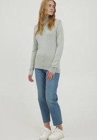 Light gray, long-sleeve turtleneck sweater with ribbed cuffs, paired with cropped blue jeans and white sneakers. Simple, casual design.