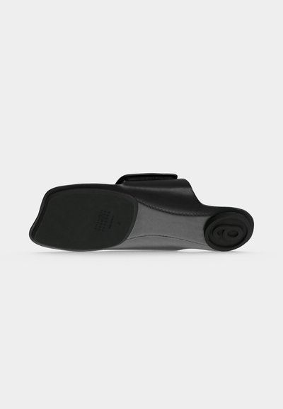 Μαύρο δερμάτινο παπούτσι τύπου slip-on, που φαίνεται από την σόλα, με τετράγωνη μύτη και στρογγυλεμένο τακούνι με ανάγλυφη κυκλική λεπτομέρεια.