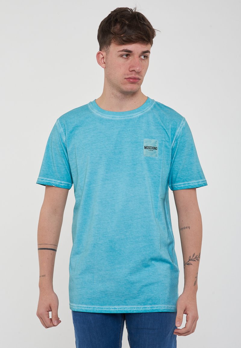 Maglietta azzurra chiara a maniche corte realizzata in un tessuto morbido. Presenta un collo rotondo e una piccola etichetta nera con logo sul lato sinistro del petto.