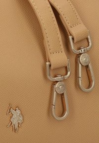 Borsa in pelle beige testurizzata con ferrature argentate, dotata di due manici superiori e di un emblema metallizzato di un giocatore di polo sul davanti.