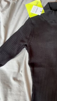Must mustriba pikae paretkätikuga must pikkade varrukatega pluus. Kangas näeb välja pehme ja veniv. Silt on nähtav kaeluse lähedal. Lamab heledal pinnal.