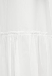 Valkoinen läpikuultava kangas, jossa on kerrostettua, rypytettyä koristepitsiä ja puoliläpinäkyvä pinta.