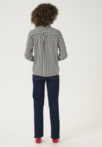 Camicia a righe bianca e nera con bottoni, jeans blu scuro e scarpe rosse. Vestibilità ampia, lunghezza media e silhouette rilassata.