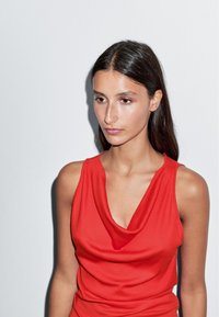 Haut sans manches rouge avec un col drapé et une texture lisse. Design simple et ajusté sans motifs ni ornements.