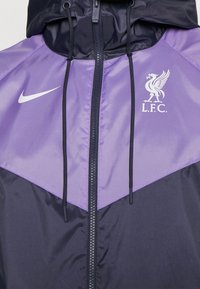 Nike purple and navy windbreaker featuring a kangaroo pocket, hood, and L.F.C. logo. Material is smooth, with adjustable drawstrings.