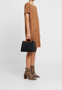 Schwarze Handtasche mit braunen Griffen, getragen zu einem braunen Wildlederkleid und braunen Ankle-Boots mit Schlangenlederdruck und Blockabsatz.