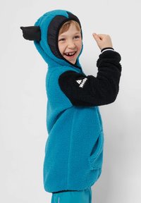 Turkos fleece-hoodie med svarta detaljer, som har en huva med örondetaljer och framfickor. Mjuk textur och avslappnad passform.