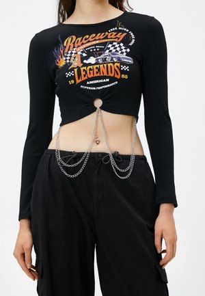 Crop top noir à manches longues avec motif de voiture de course, détails en chaîne métallique suspendus au trou central, associé à un pantalon noir taille haute.