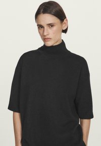 Maglione a collo alto nero a maniche corte in una morbida texture, con una vestibilità rilassata, colletto a coste e design minimalista.