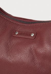 Bolso de piel burdeos con una superficie texturizada, costuras visibles y un cierre de cremallera metálica con una etiqueta de la marca.