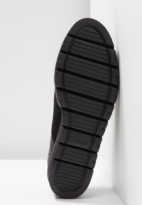 Semelle de chaussure en caoutchouc noir avec des rainures texturées et un logo subtil. Le matériau présente des accents lisses et doux autour des bords.