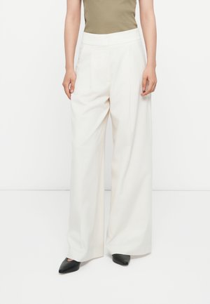 Witte wijde broek met een gladde textuur, voorzien van een hoge tailleband en scherpe voorplooien, gecombineerd met zwarte puntige schoenen.