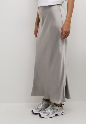 Gonna maxi in satin grigio con una texture sottile, caratterizzata da un taglio dritto e uno spacco laterale, abbinata a scarpe da ginnastica bianche e grigie.